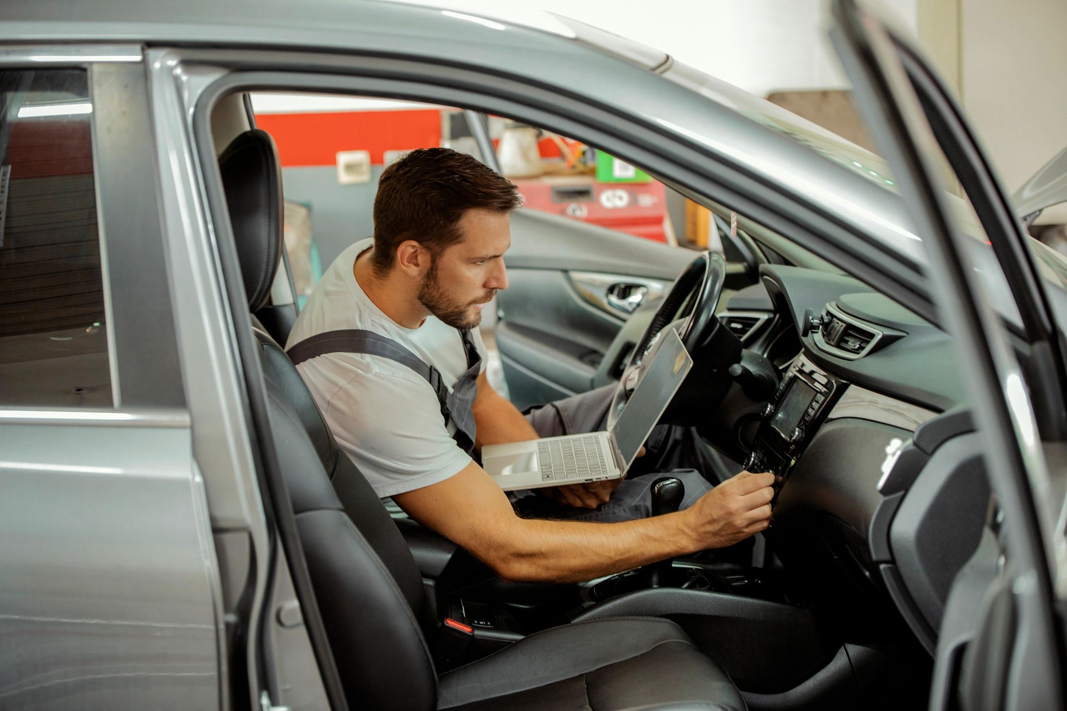 Mechanic using a laptop to run vehicle diagnostics in an auto repair bay.